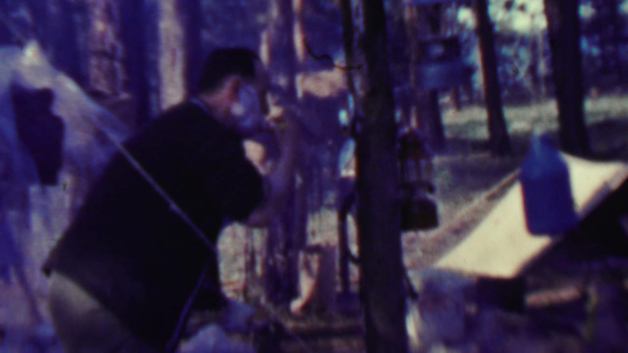 Man leaning forward among trees with tent and campsite gear nearby.