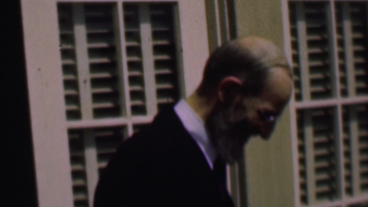 Older man in profile looking downward near shuttered windows.