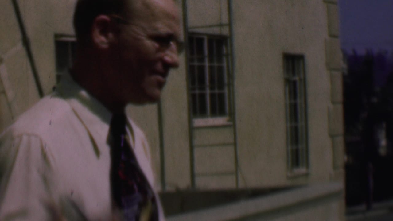 Close side view of a man in a light shirt and tie near a sunlit building wall.