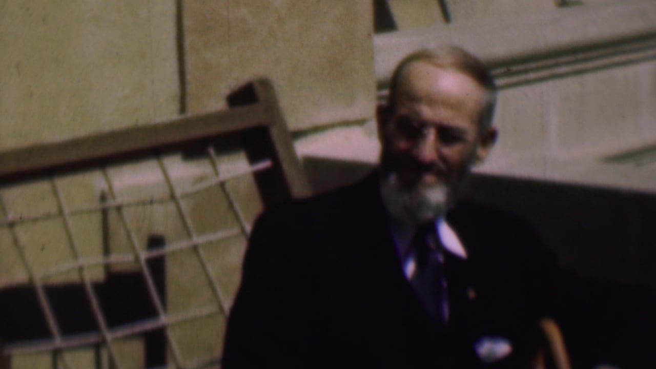 Bearded man in a suit smiling near a tilted grid-patterned structure.