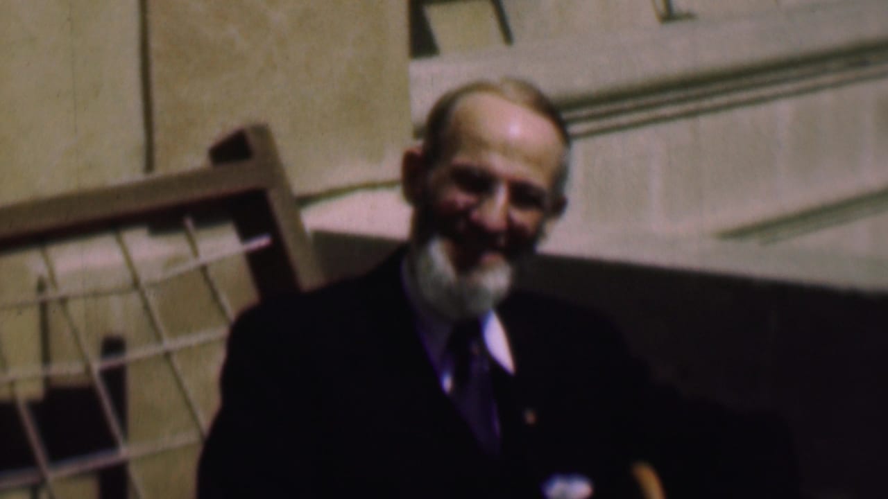 Smiling older man in a suit faces the camera outdoors.