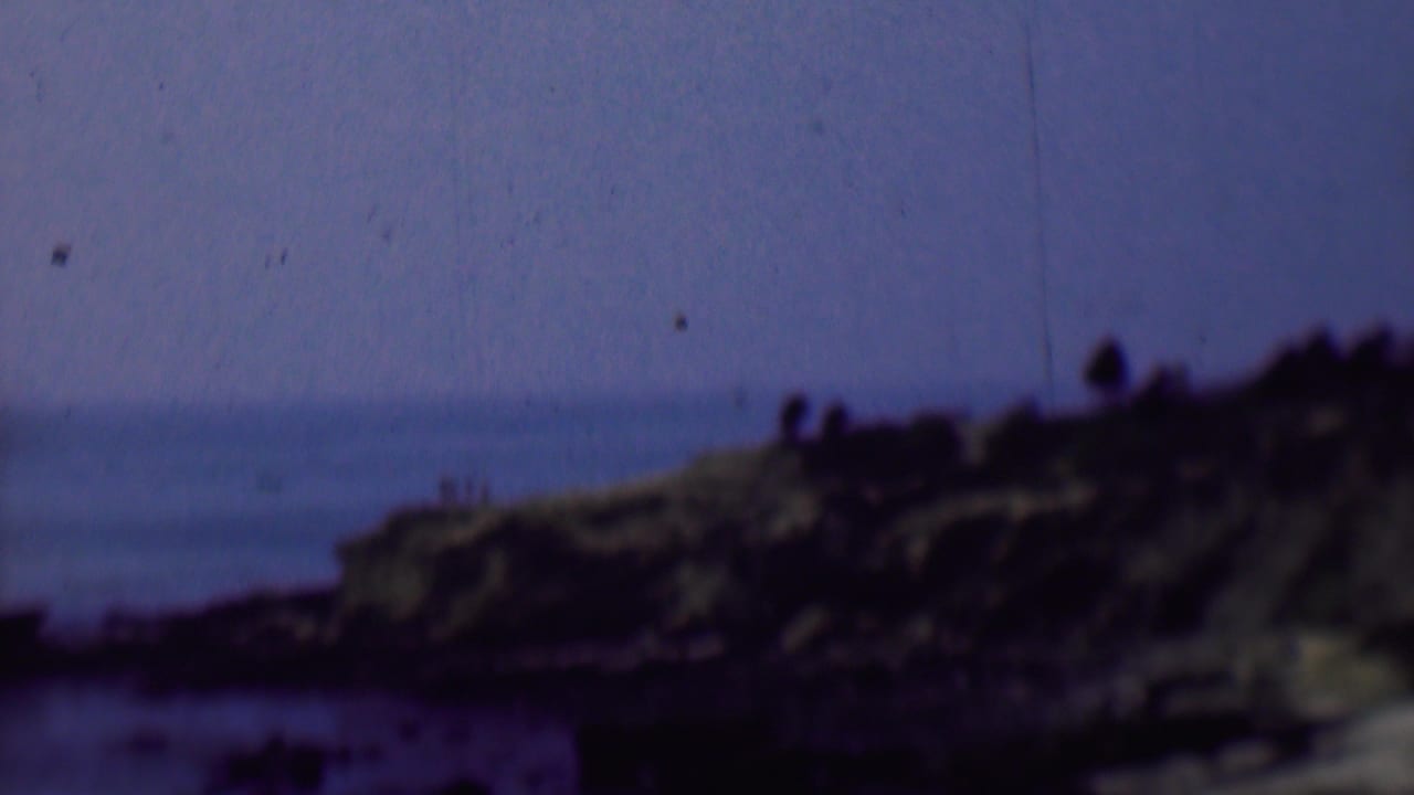 Coastal bluff beside the ocean with dark rocks and distant people along the ridge.