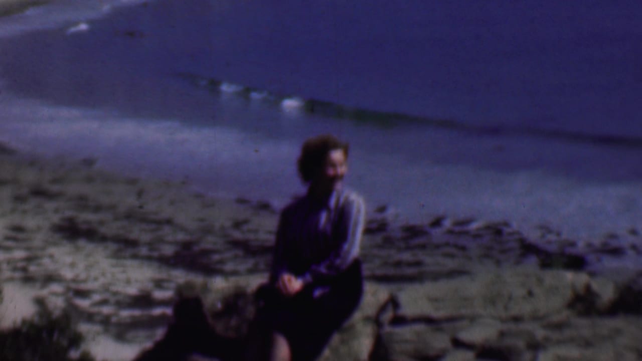 Woman seated on rocks near a sandy beach and ocean waves.