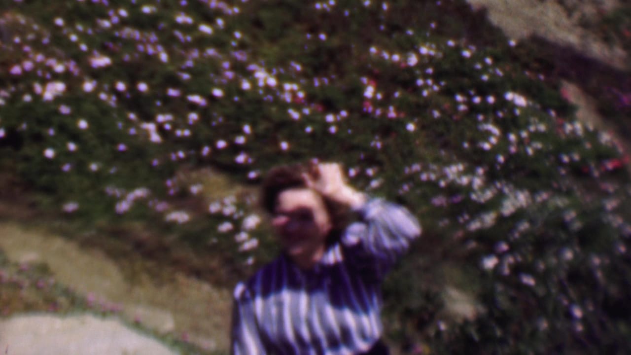 Woman in a striped shirt waves beside a flowering hillside path.