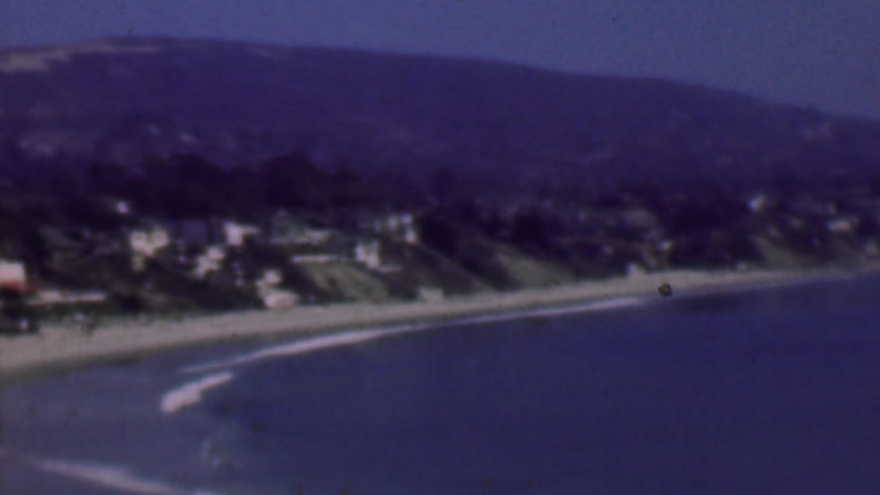 Coastline with beach, surf, hillside buildings, and open water.