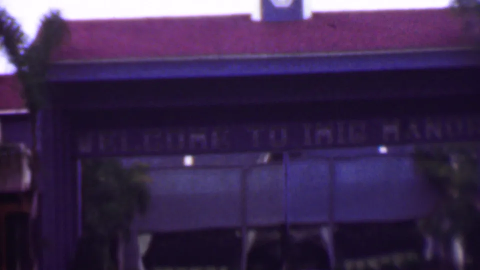 Final 1961 8mm frame holds on the building facade, where faded welcome lettering, a red roof, palm trees, and shaded awnings remain visible despite motion softness.