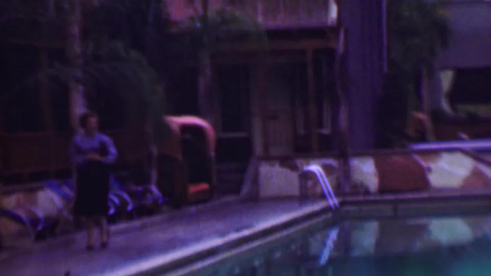 The woman continues past lounge chairs beside the swimming pool, with palms and a wooden resort-like building visible in the 1961 San Diego footage.