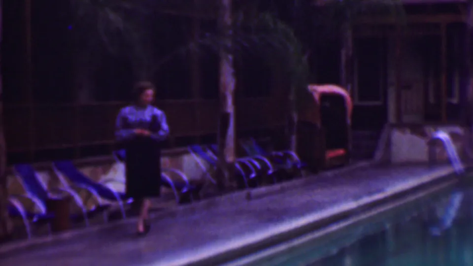 The woman walks along the pool deck in the San Diego resort setting, passing rows of lounge chairs with the pool occupying the foreground.