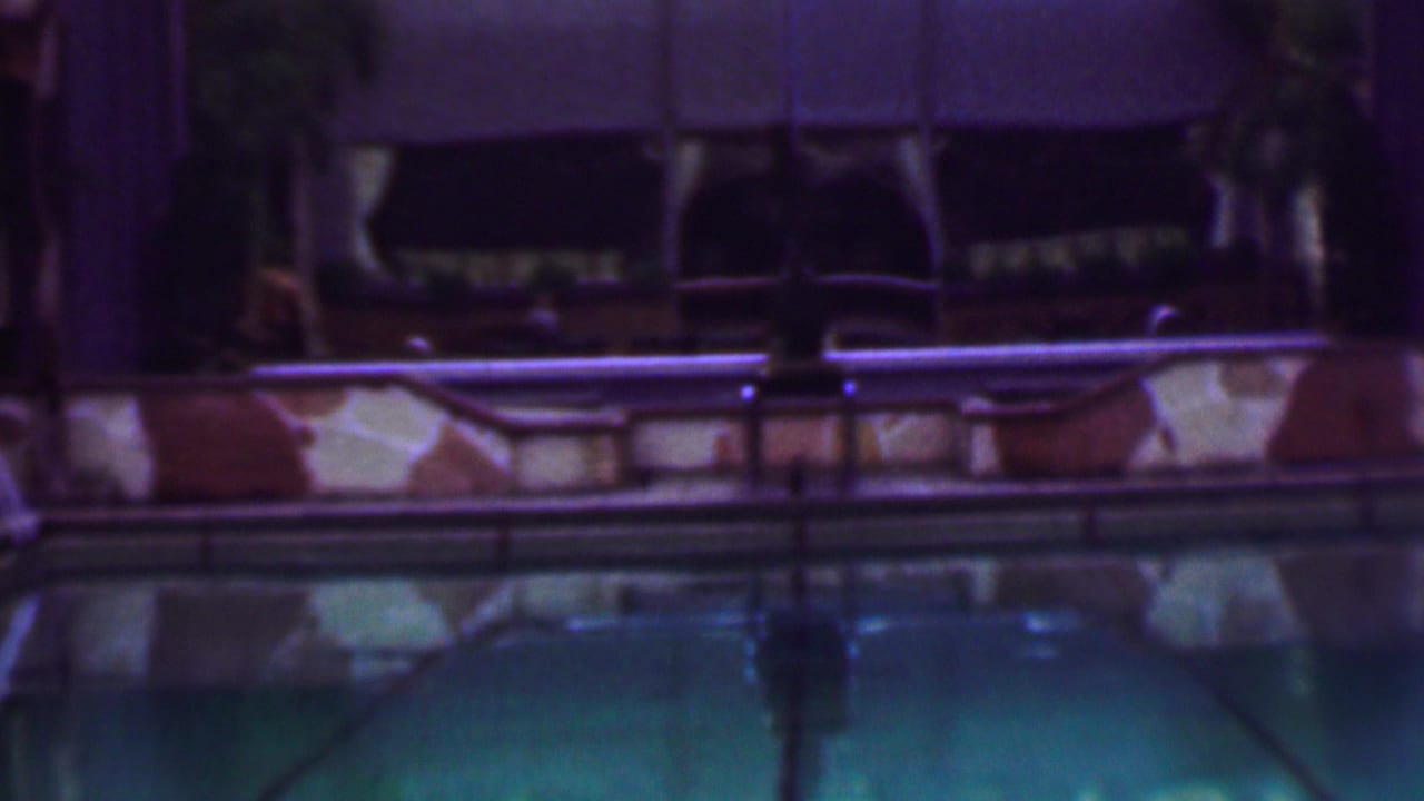1961 San Diego home-movie frame showing a quiet nighttime pool area with turquoise water, stone pool edging, railings, and shadowed building details in the background.