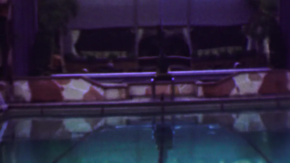 1961 San Diego home-movie frame showing a quiet nighttime pool area with turquoise water, stone pool edging, railings, and shadowed building details in the background.