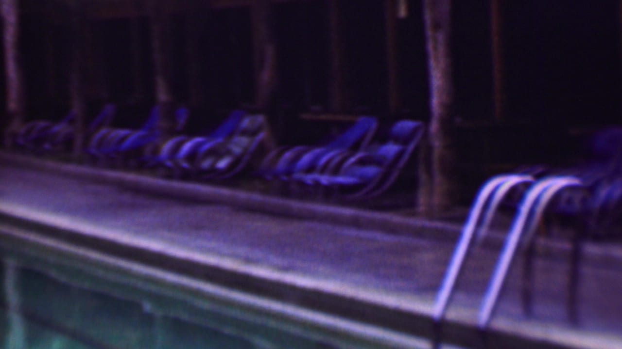 1961 San Diego home-movie frame showing a swimming pool edge, rows of blue lounge chairs, and a dim patio area with soft 8mm color shift.