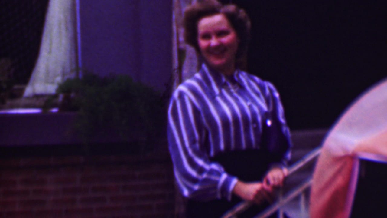 Woman standing and smiling beside patio railing and plants.