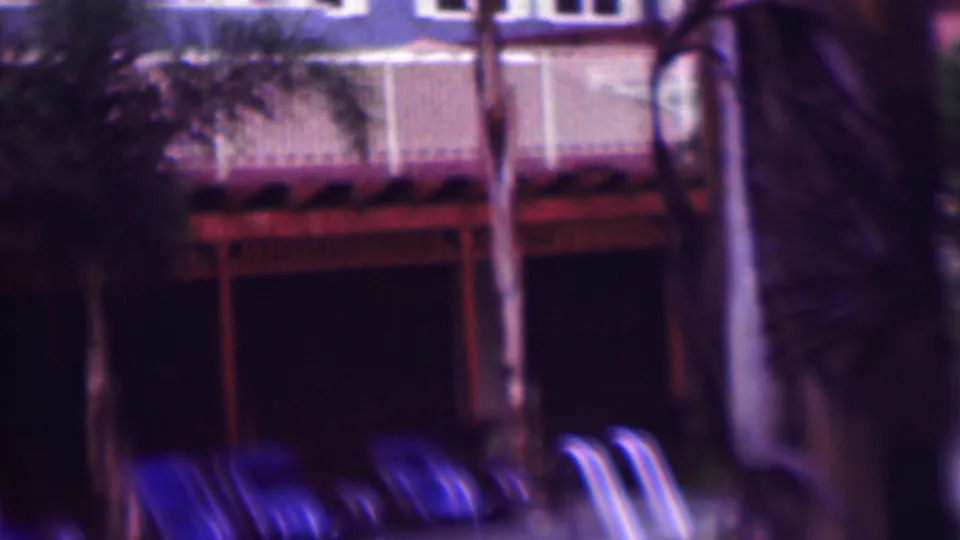 Soft, dark 8mm frame from San Diego showing blue lounge chairs, palm trunks, white railings, and a residential building exterior near a pool area.