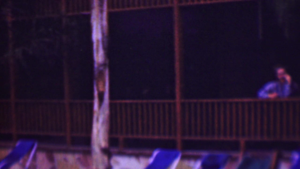 Upper balcony with a person at the right and a curved poolside structure below.
