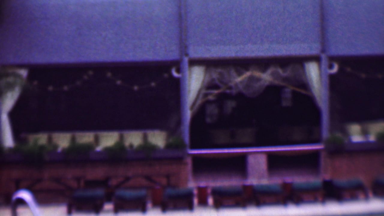 Exterior facade with curtained windows, string lights, planter boxes, and lounge chairs in front.
