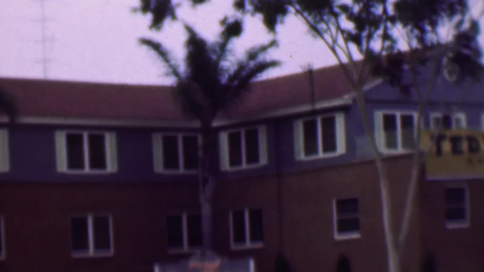 Final 1961 San Diego frame with the blue-and-brown building, rows of white-trimmed windows, foreground trees, and the Ted Fio Rito banner mostly cropped on the right.