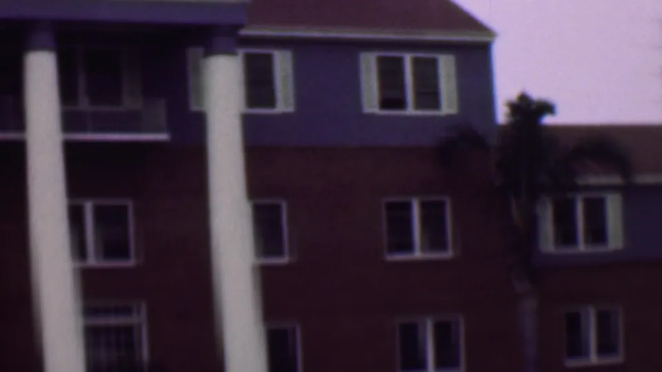 1961 San Diego exterior frame centered on a building entrance area with two tall white columns, red and blue facade sections, white-framed windows, and palms nearby.