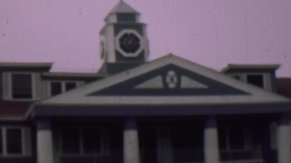 1961 San Diego home-movie frame showing the roofline of the columned building with a triangular gable, dormer windows, and a small clock or tower feature above the roof.