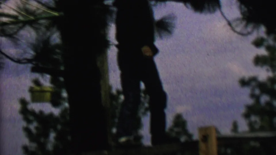 A silhouetted person appears to shift position on or near the wooden fence in this low-light 8mm frame from metadata-supported 1962 St. Paul, Minnesota.