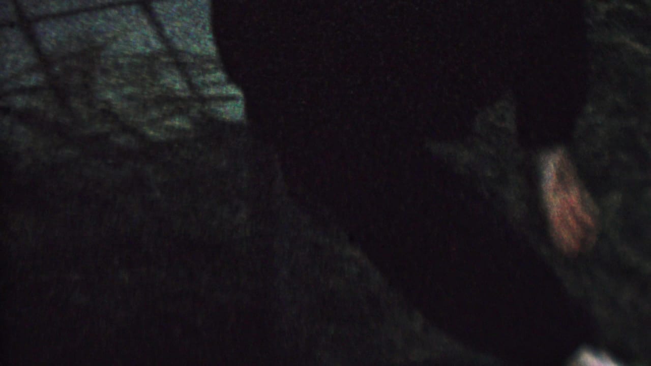 1962 8mm home-movie frame showing a child in dark clothing hanging upside down in a shadowed outdoor setting, with the face partly visible.