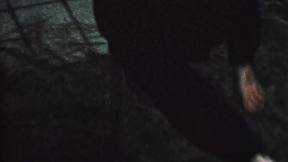 1962 8mm home-movie frame showing a child in dark clothing hanging upside down in a shadowed outdoor setting, with the face partly visible.