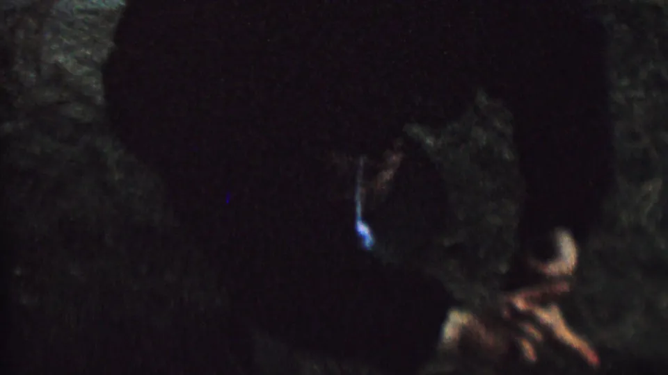 Shadowy 1962 home-movie frame with a child’s partially illuminated face appearing upside down against a dark outdoor background.