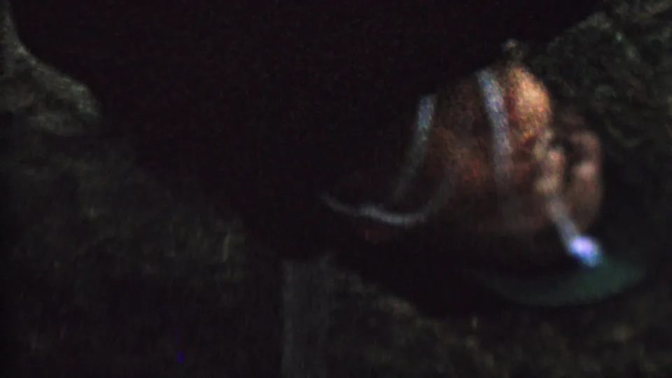 Close 8mm frame of a child hanging upside down, with a blue cord or rope-like line near the head and dark grass or foliage behind.