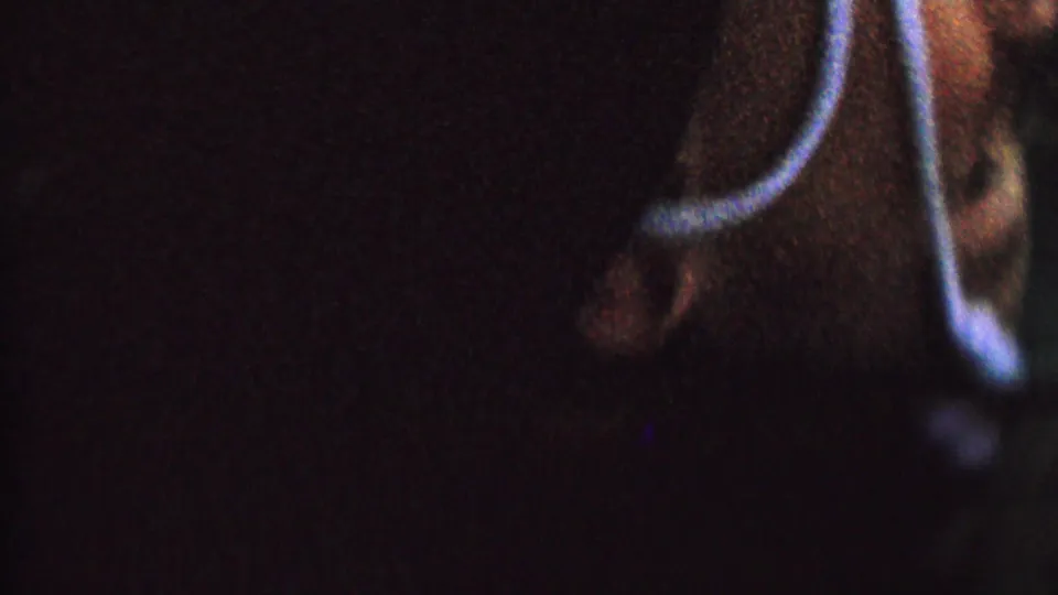 Dim 1962 8mm frame showing the child close to camera, upside down in dark clothing, with a blue cord and a hand visible at the edge.