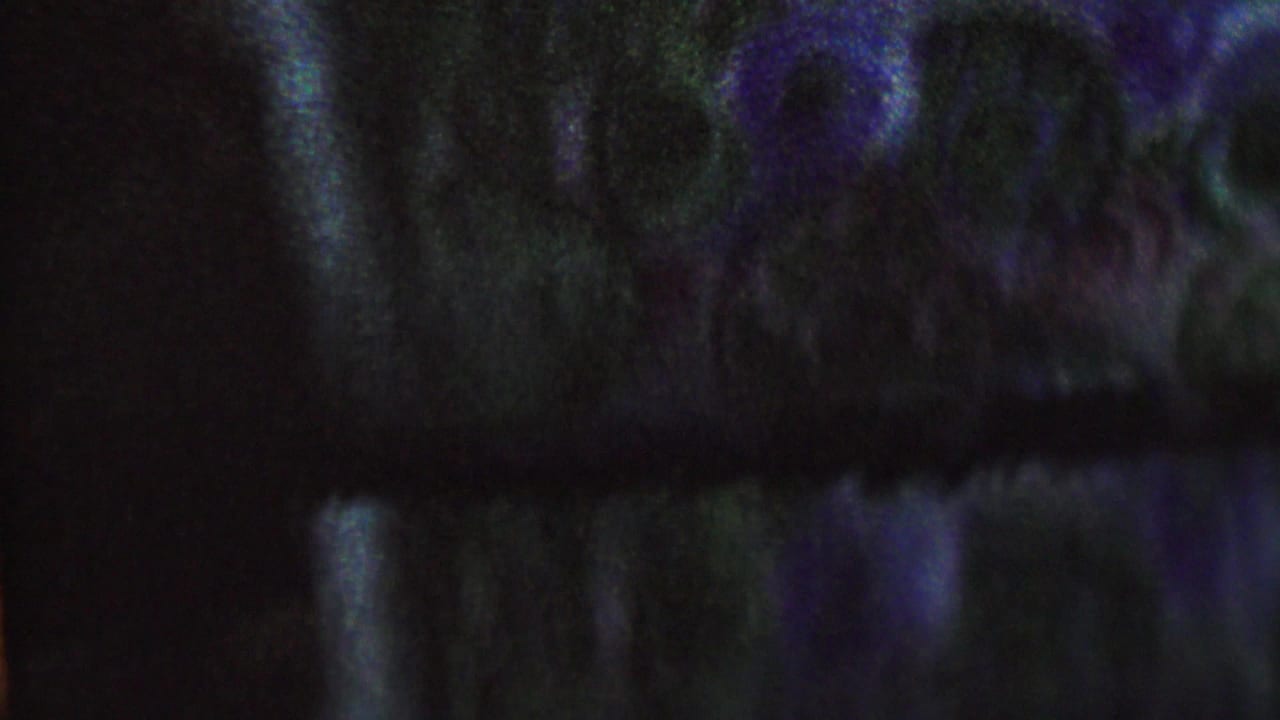 Dark blurred frame with blue and purple light across indistinct shapes.