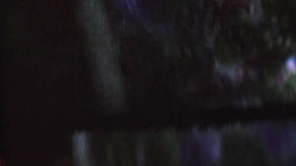 The frame remains very dark and motion-blurred, showing faint vertical forms, colored speckling, and little identifiable context beyond the 8mm texture.