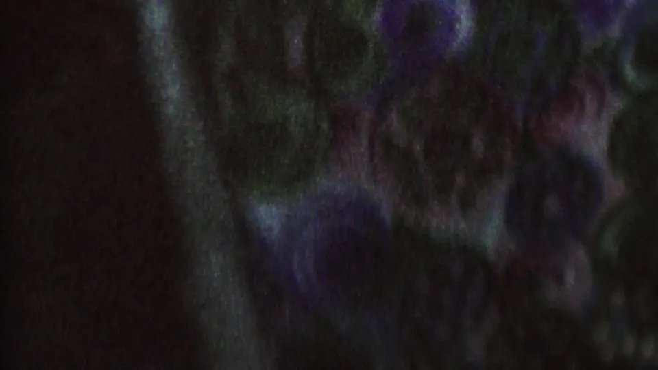 Soft, grainy 1962 8mm frame from the St. Paul clip with a dark-clothed adult near another partially visible figure in an ambiguous dramatic setup.