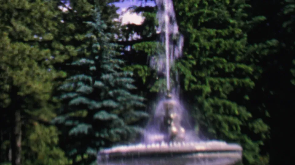 1962 St. Paul park footage showing the fountain from a slightly shifted angle, with water spray and evergreen branches filling the background.