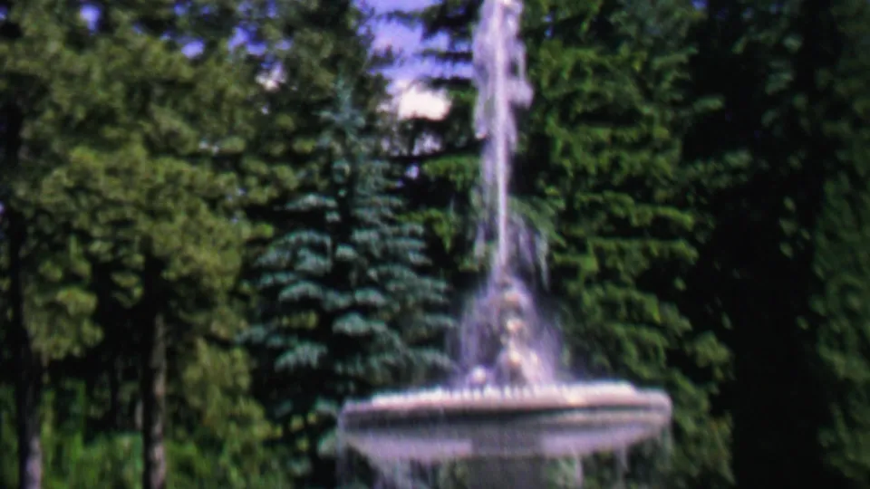 1962 home-movie view of the fountain in a landscaped St. Paul park, with the basin low in frame and water rising in front of trees.