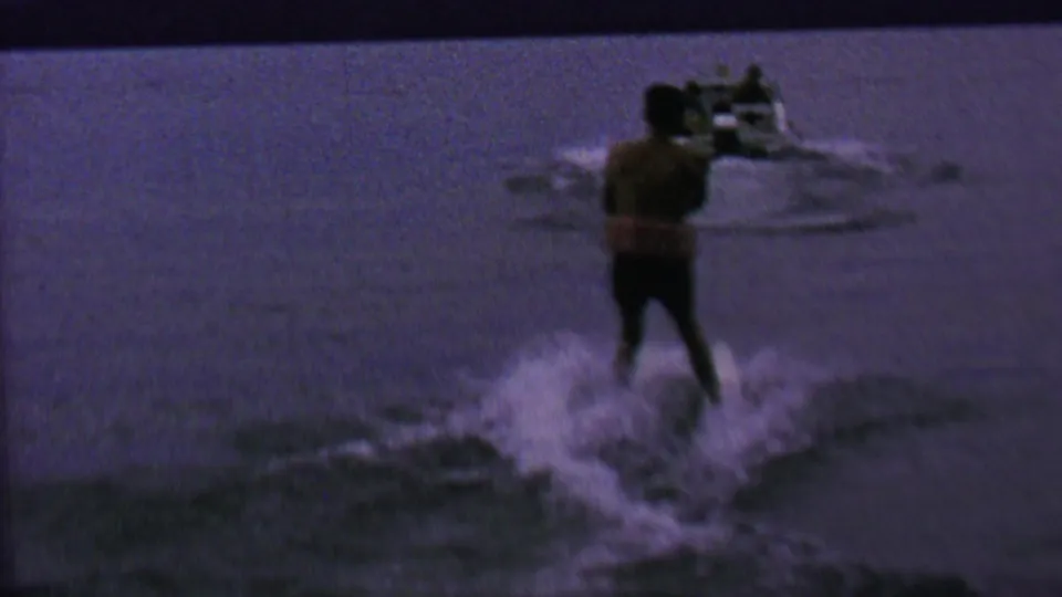 Final 1962 St. Paul home-movie frame showing a distant person from behind moving through shallow water near the fountain spray.