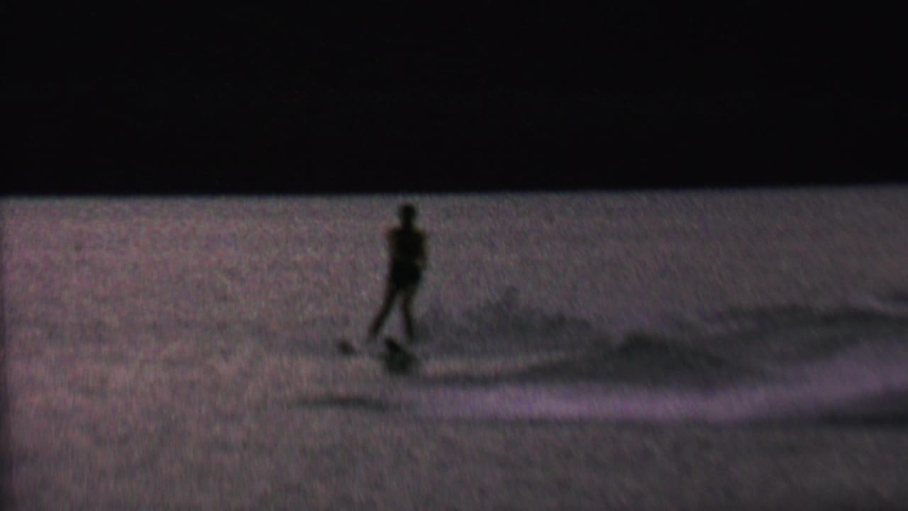 A silhouetted male water skier is pulled across the rippled lake surface, with the tow line and wake visible in low evening light.