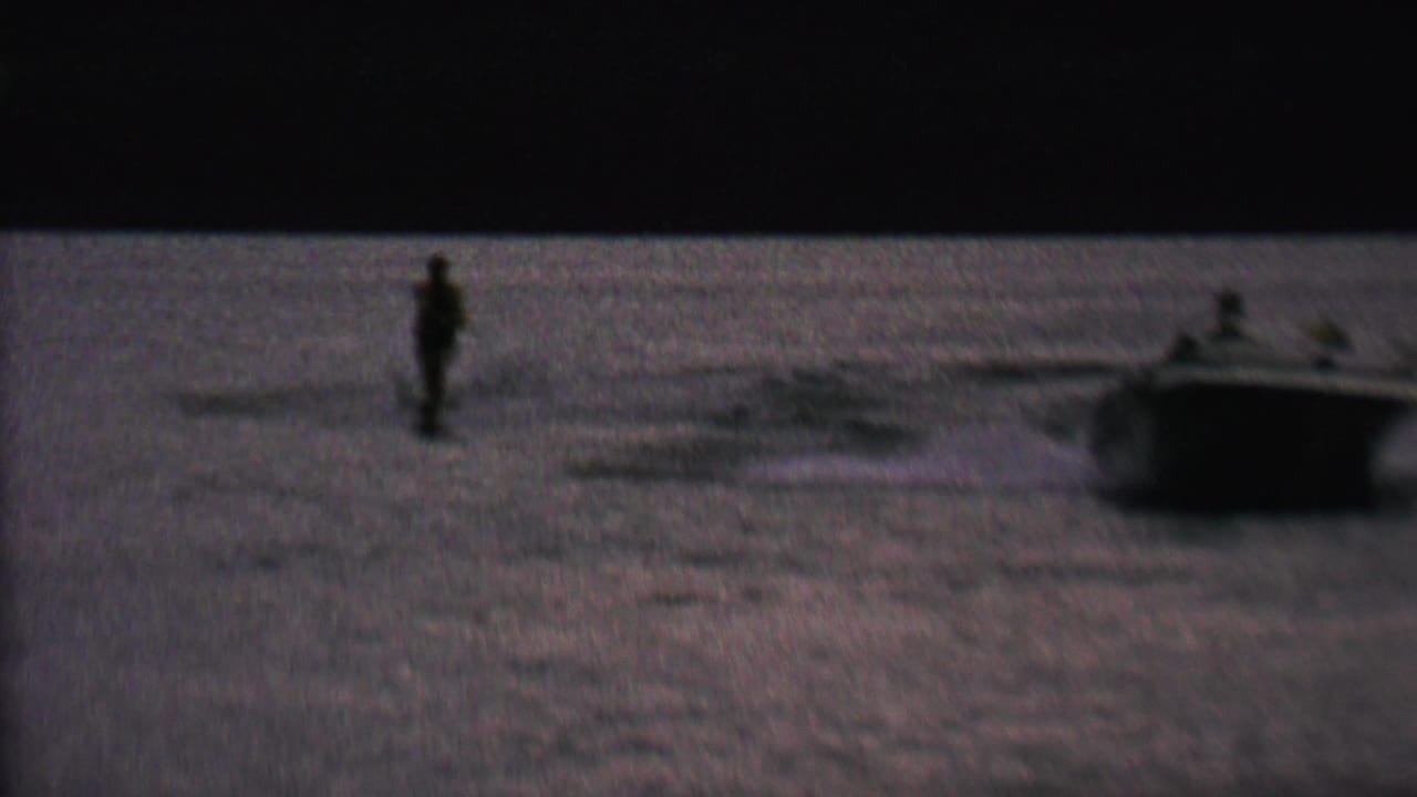 A distant man water skis on a lake near a small boat in supplied 1962 St. Paul, Minnesota home-movie footage, seen in grainy low evening light.