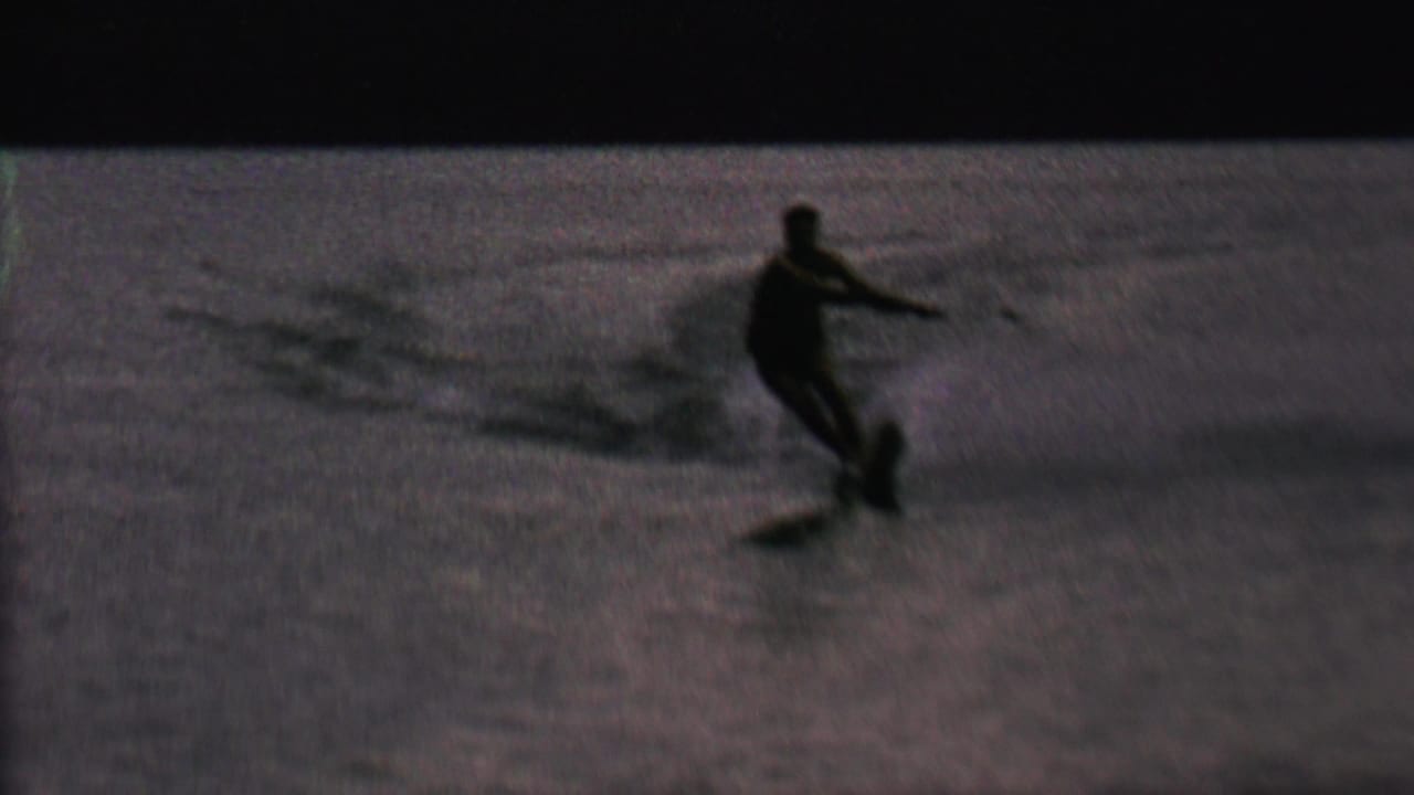 In 1962 home-movie footage from St. Paul, Minnesota, an adult water skier appears in silhouette on rippled lake water while holding a tow rope.