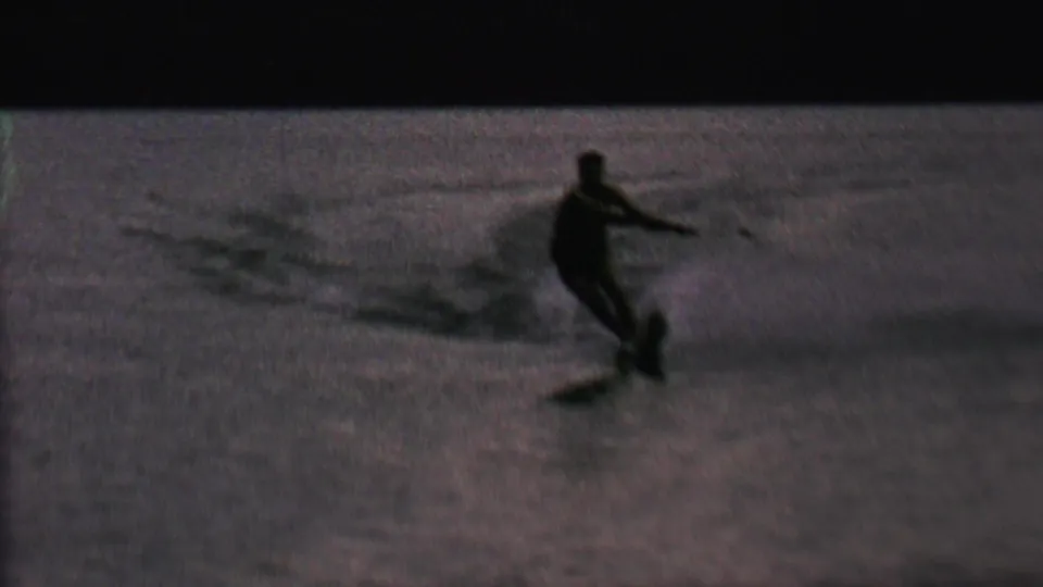 In 1962 home-movie footage from St. Paul, Minnesota, an adult water skier appears in silhouette on rippled lake water while holding a tow rope.