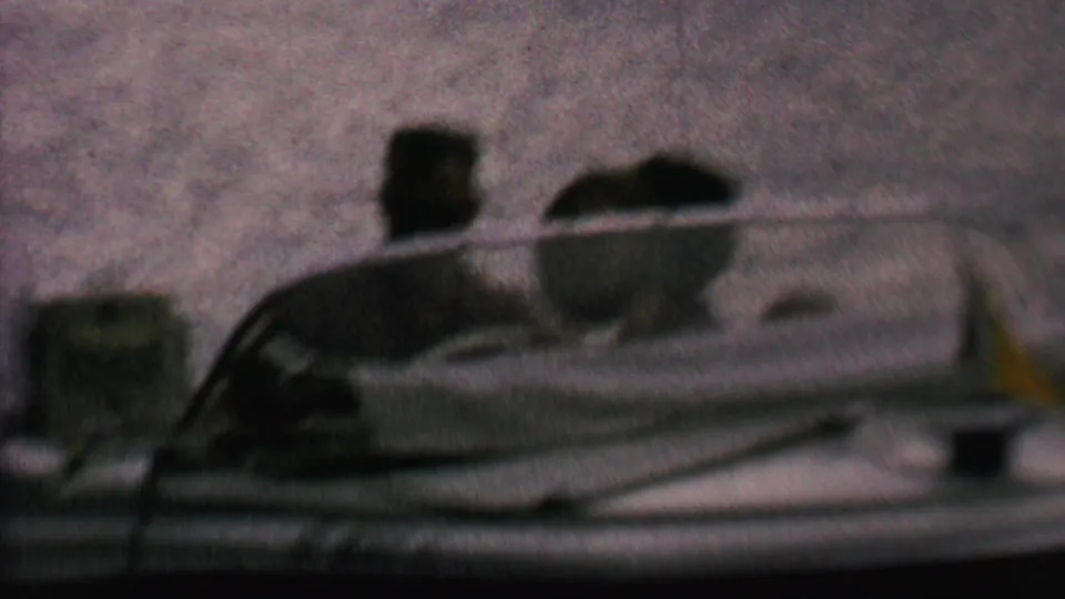 A small open motorboat sits on reflective lake water, with seated people visible in soft, low-light 8mm footage from the supplied 1962 clip metadata.