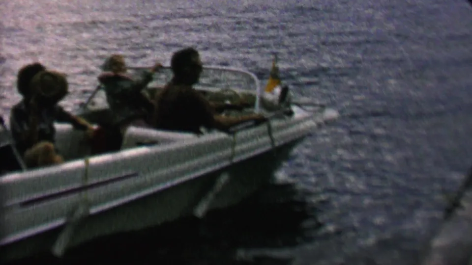1962 St. Paul home-movie frame from metadata showing passengers clustered in a small motorboat on open water, with one figure raising an arm or object as the boat faces the camera.