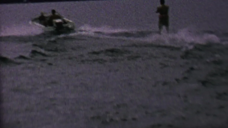 The motorboat and skier separate across the frame as wake spreads over the lake, in a grainy 8mm home-movie view tied to the supplied 1962 St. Paul metadata.