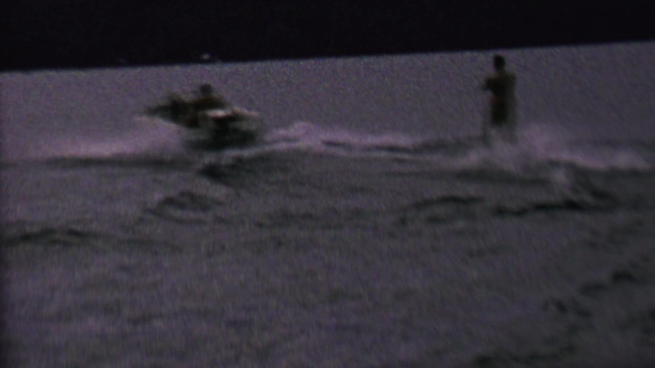 In 1962 home-movie footage from the St. Paul, Minnesota area, a small motorboat pulls a distant water skier across a dark, grainy lake surface.