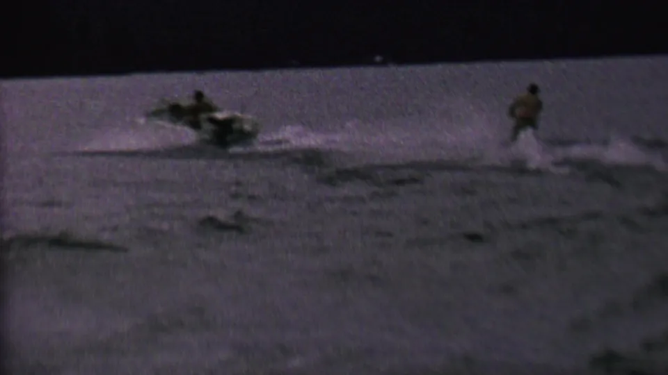 A distant water skier follows a motorboat across open water in grainy 1962 8mm footage associated with St. Paul, Minnesota.