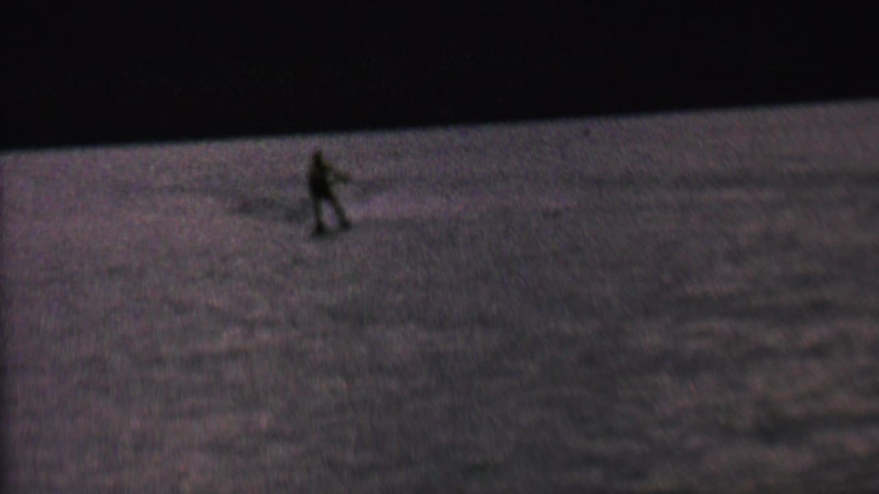 A distant water skier moves across dark reflective lake water in grainy 8mm footage associated with 1962 St. Paul, Minnesota metadata.