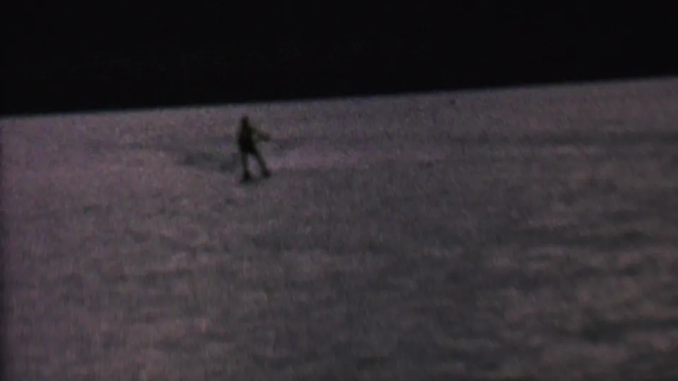 A distant water skier moves across dark reflective lake water in grainy 8mm footage associated with 1962 St. Paul, Minnesota metadata.