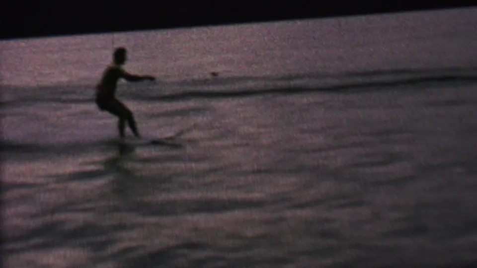 A closer silhouetted water skier rides across calm lake water, leaving a visible wake in the supplied 1962 St. Paul recreation clip.