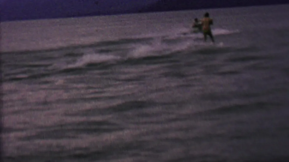 A small motorboat pulls the woman on water skis through gentle wake, seen in grainy 8mm footage identified by metadata as St. Paul, Minnesota in 1962.