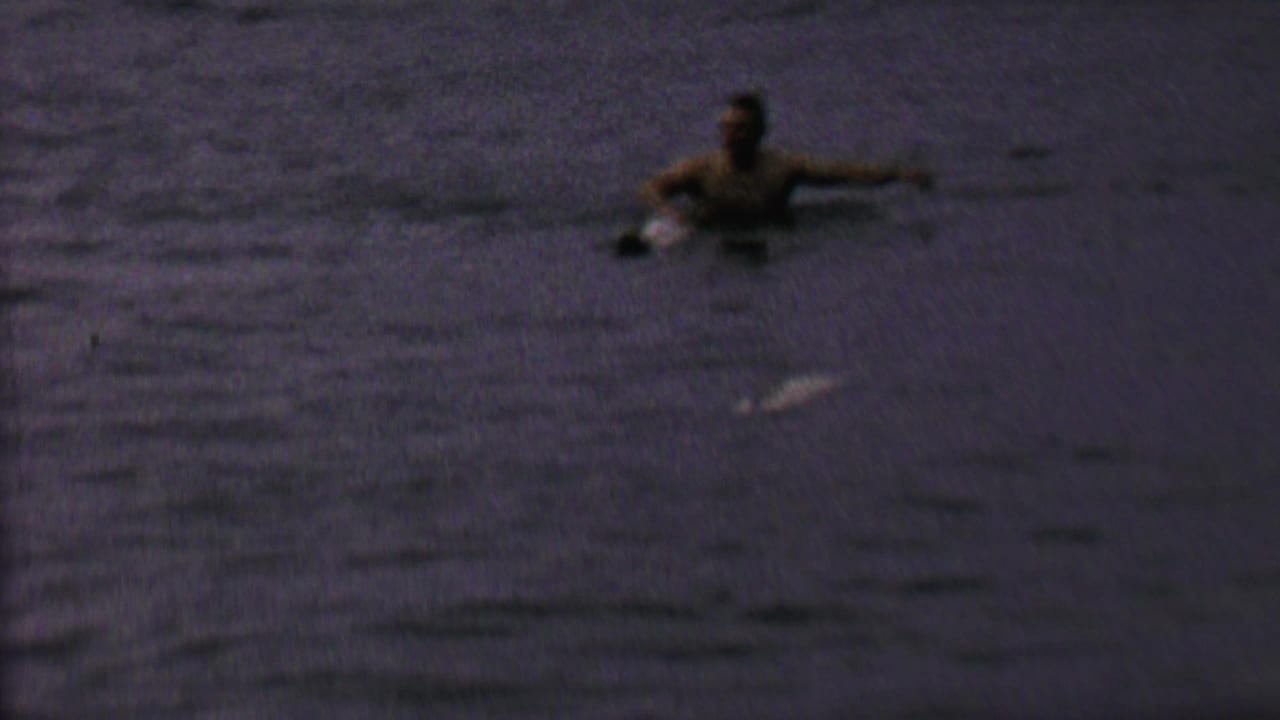 Person floating or swimming in dark lake water with arms extended.