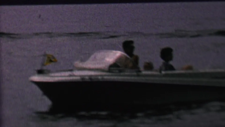 A small motorboat carrying several people crosses dark lake water in the supplied 1962 United States home-movie footage.