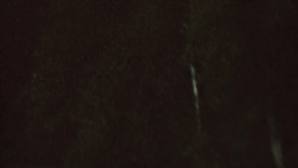 The frame is very dark, with faint traces of water, possible tow line, and low-light film noise visible from the nighttime water skiing scene.